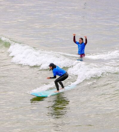 Image of female blind surfer catching a wave with guide in the background cheering her on